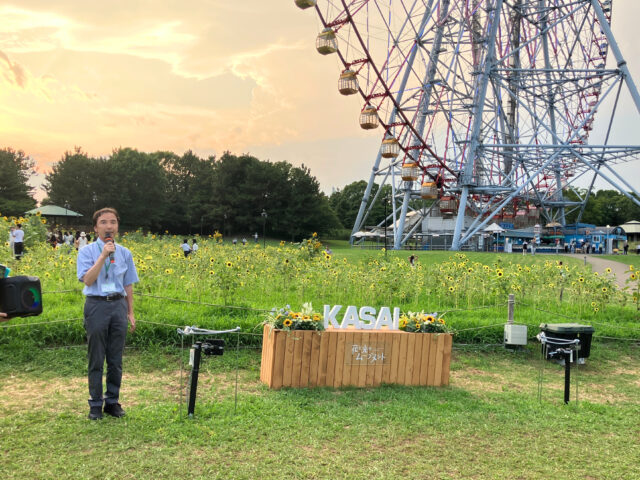 点灯式で挨拶する松井公園長。後ろにはひまわり畑と大観覧車